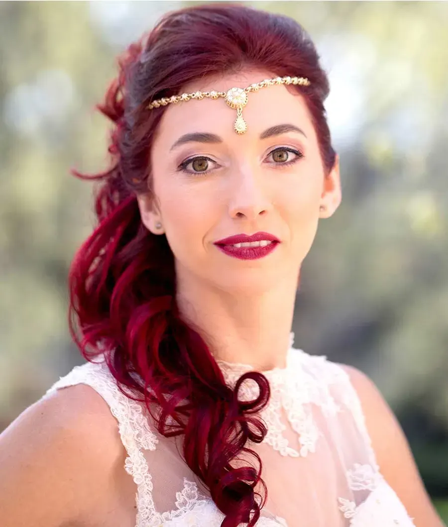 Mariée aux longs cheveux rouges bouclés ramenés sur l'épaule, bijou de front doré
