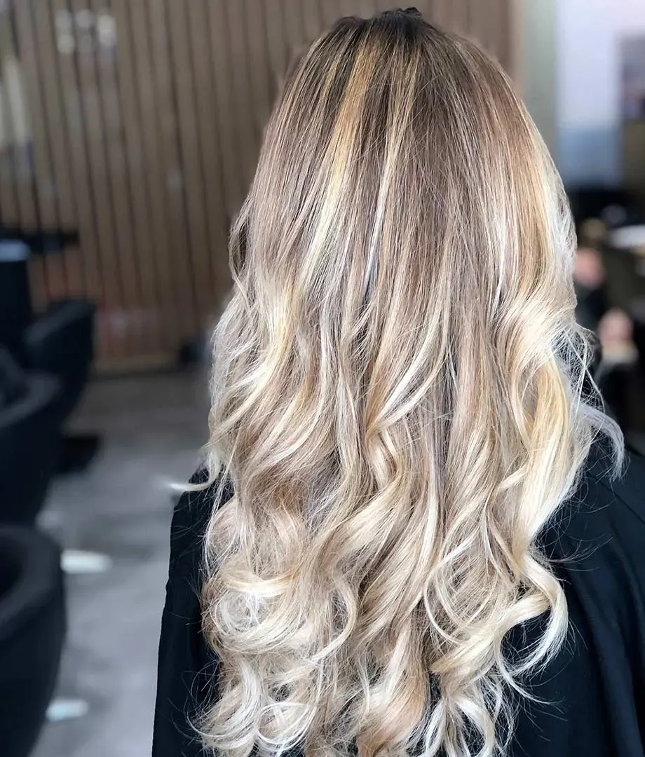 Mèches blond polaire sur cheveux longs bouclés